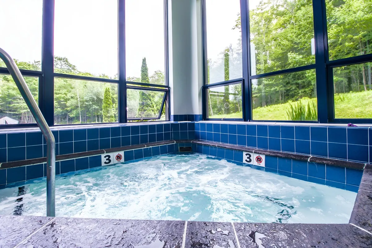 An interior shot of a tranquil jacuzzi area with large windows framing natural surroundings. Warm light streams in, inviting guests to relax and unwind after an active day outdoors.