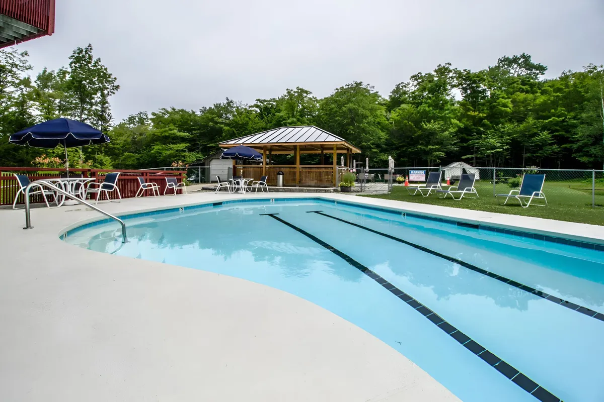 An inviting outdoor swimming pool with a gazebo, surrounded by trees and poolside chairs. The scene suggests both leisurely swims and social gatherings in a beautiful natural setting.