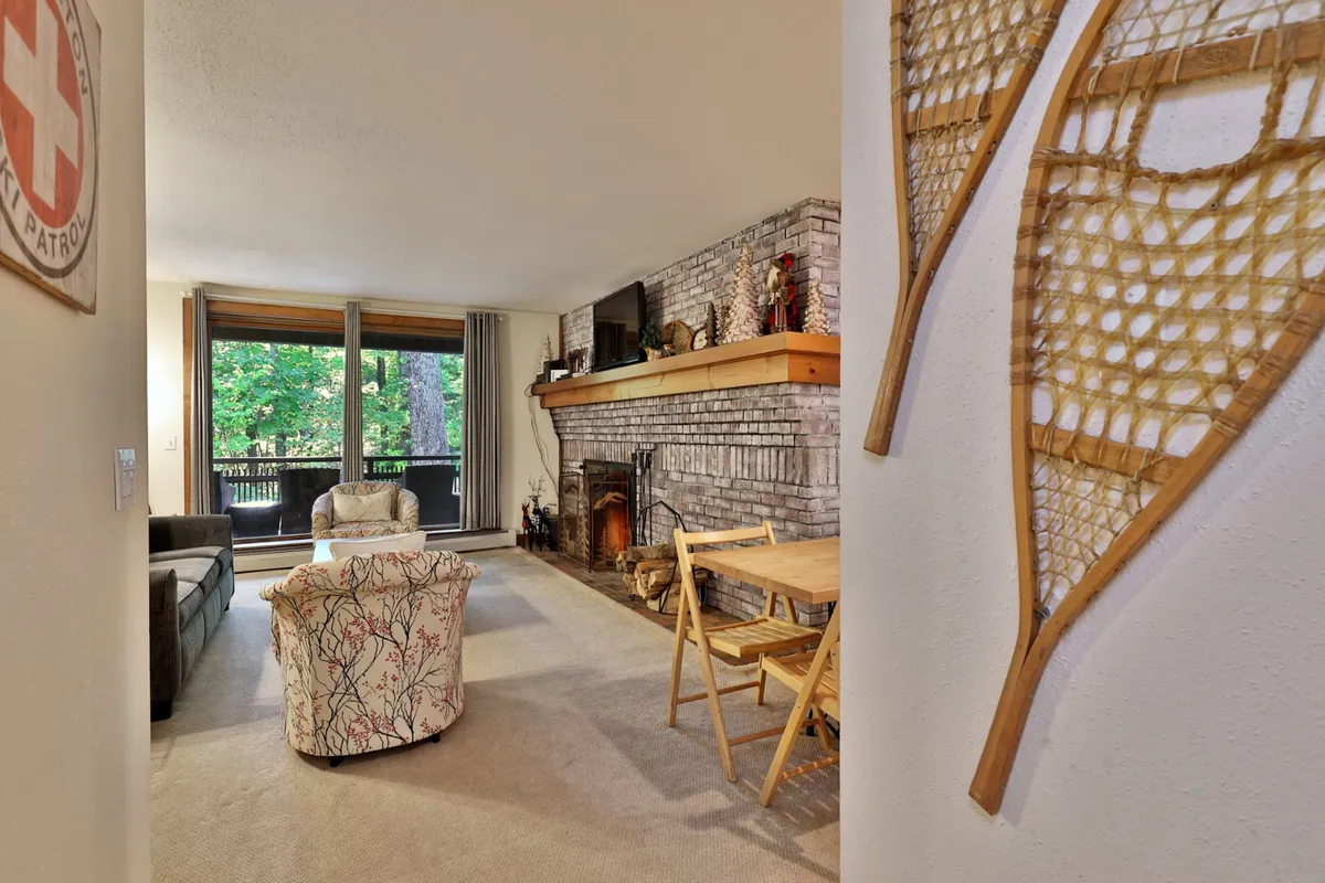 A cozy living room with a fireplace as the focal point, surrounded by comfortable seating including a sofa and armchairs. The wooden mantle adds rustic charm, while a window offers a glimpse of the outdoors. The space invites relaxation and socializing, with the TV positioned for entertainment and ample room for gathering.