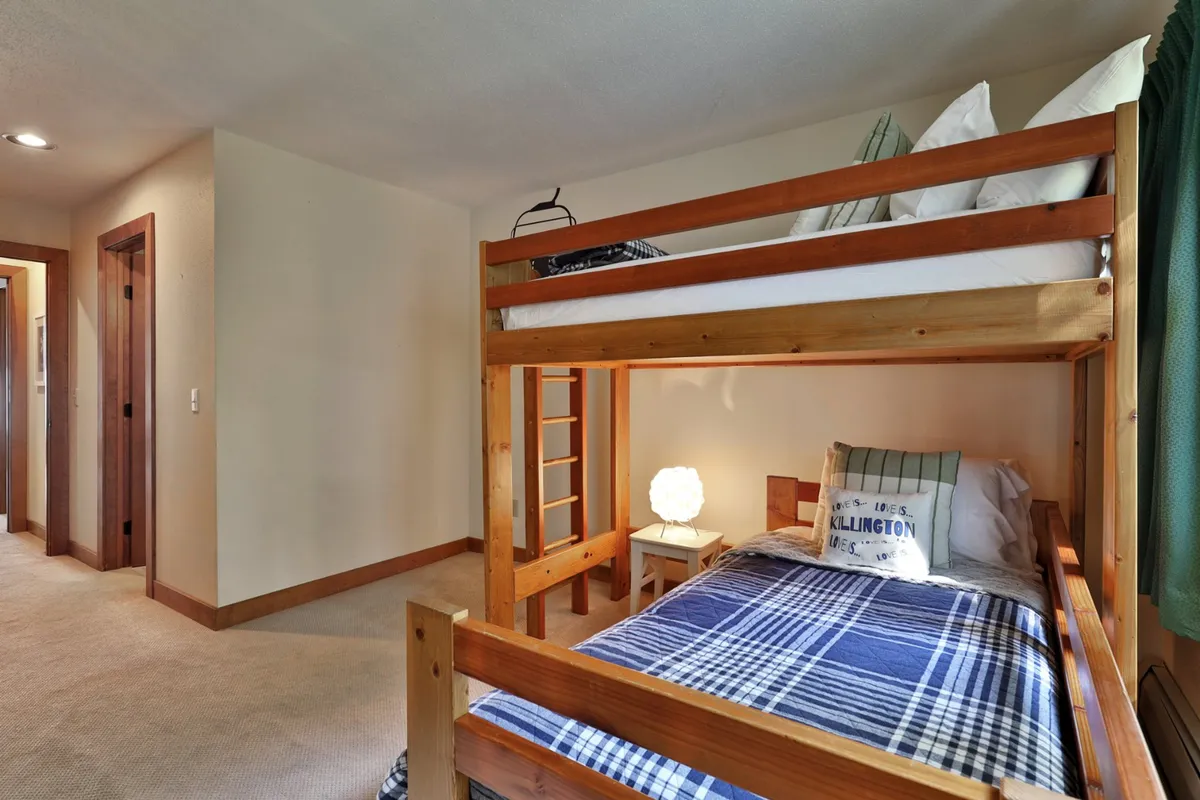 A playful, cozy bunk bed setup with plaid bedding and a lamp, inviting children to imagine adventure and shared memories. The ladder adds a sense of fun and excitement, perfect for young guests.