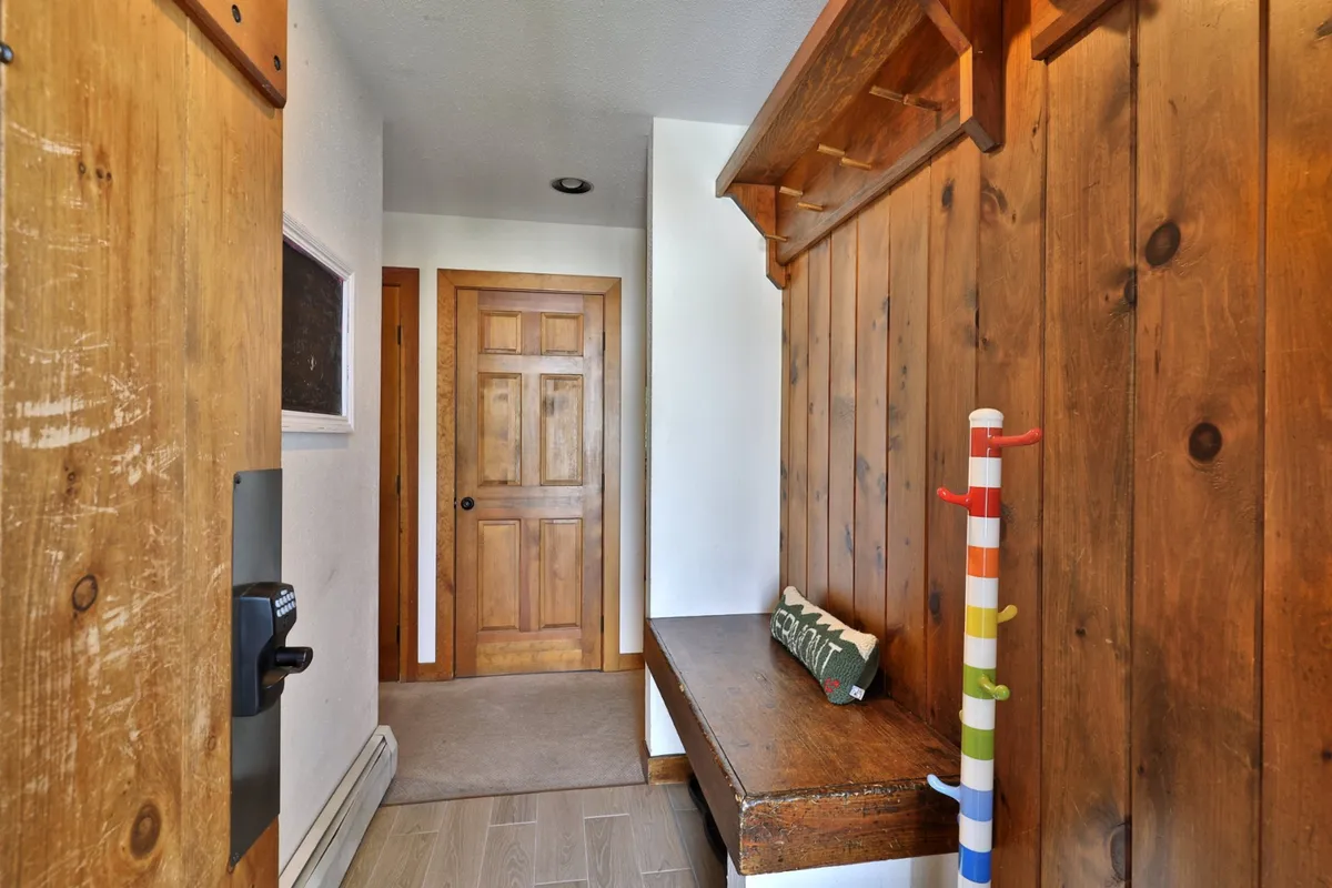 The entry hall displays a wooden bench, a colorful coat rack, and a textured wall, evoking a sense of warmth and hospitality. The area is designed for storing outdoor gear and provides a comfortable transition into the home.