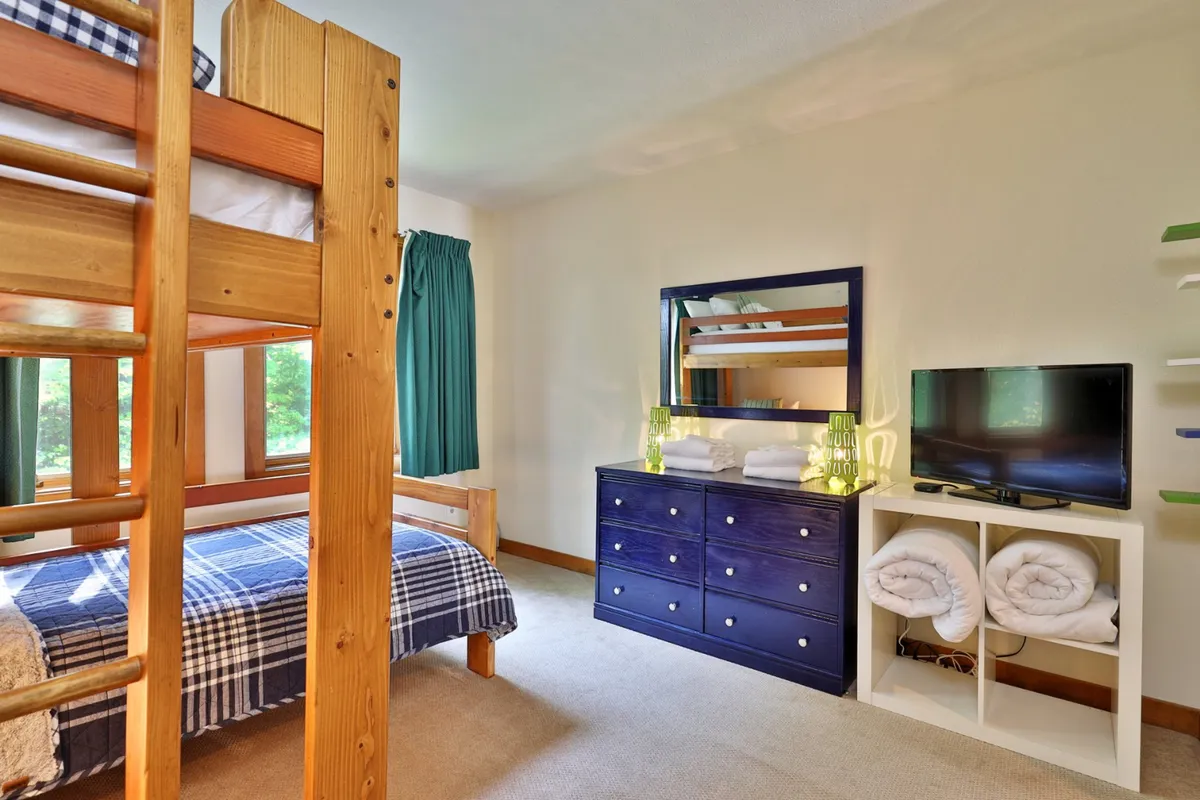A family-friendly bedroom featuring a bunk bed with ladder access, a dresser, TV, and mirror. The cozy setup is ideal for kids or friends, with space for both play and relaxation.