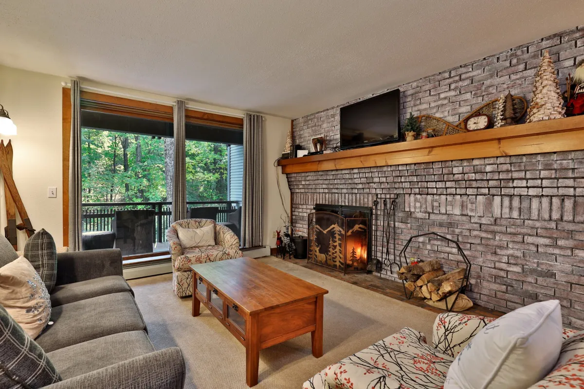 The living area features a central fireplace, a coffee table, and expansive windows with treetop views. The space invites relaxation, socializing, and enjoying the warmth and tranquility of the retreat.