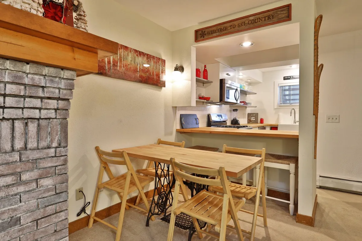 An open-concept space where a wooden dining table sits next to a stone fireplace, with a view into the kitchen featuring modern appliances. A welcome sign adds a homely touch, making the space feel inviting for shared meals and festive gatherings.