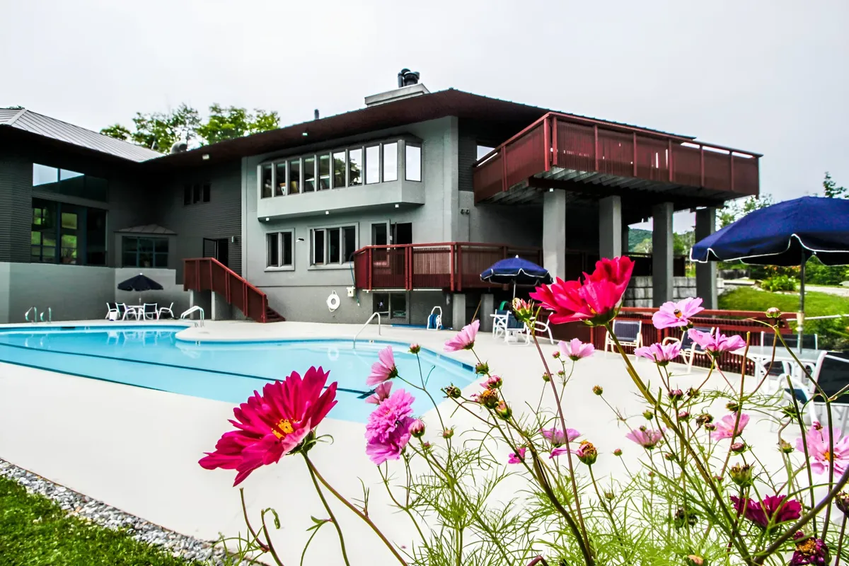 An inviting outdoor swimming pool surrounded by a flower garden, deck area with lounge chairs, and a charming building facade in the background. The scene is lively yet relaxing, ideal for warm-weather fun and family gatherings.