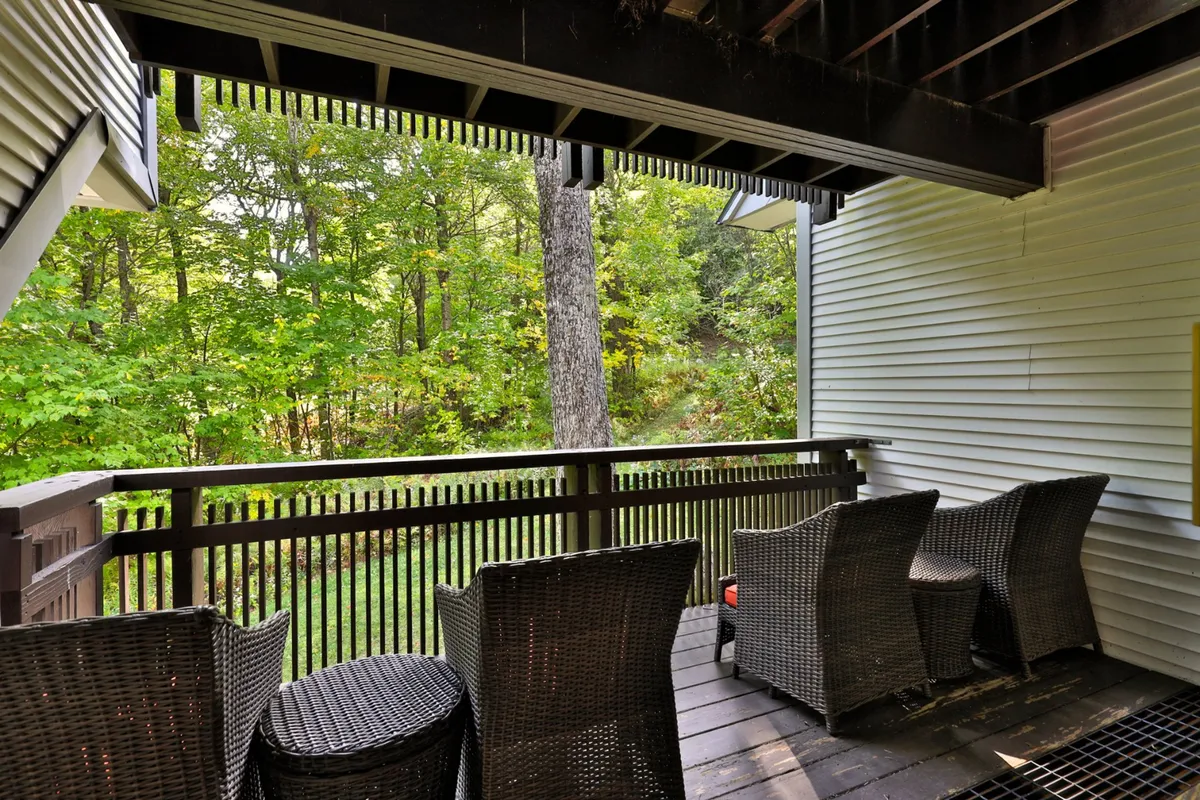 An inviting porch scene with wicker chairs and wooden railing, surrounded by lush greenery. The space suggests a comfortable spot for friends to gather, relax, and enjoy the evening air before or after hitting local hotspots.