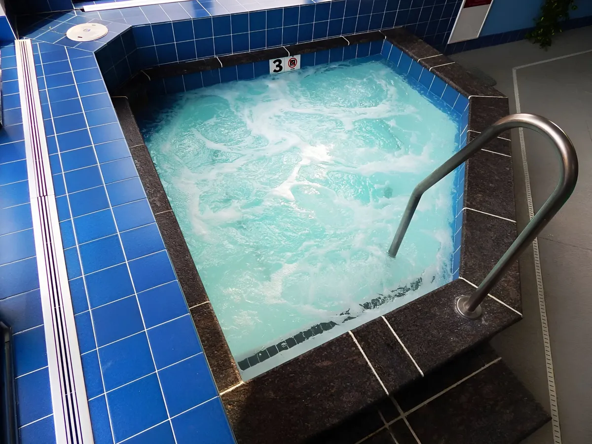 The tranquil interior scene showcases a whirlpool with blue tiles and stainless steel railing, offering a glimpse into the resort's amenity center where guests can unwind and socialize after a day on the slopes.